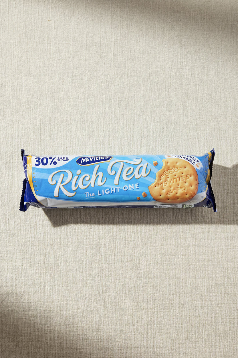 A package of McVities Rich Tea The Light One biscuits, showing the blue and white packaging with a picture of the biscuit on a light wood grain surface.