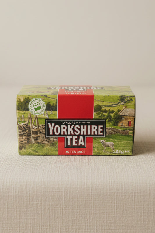 A box of Taylor's of Harrogate Yorkshire Tea resting on a gray textured fabric surface, with a blurred indoor background.